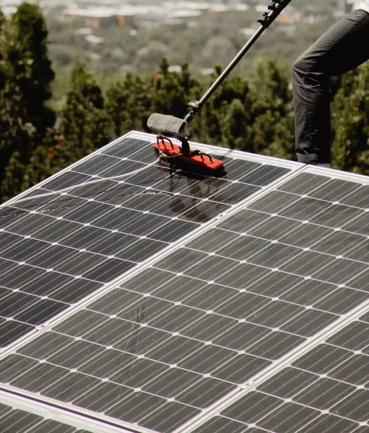 Technician cleaning solar panels with a long-handled brush